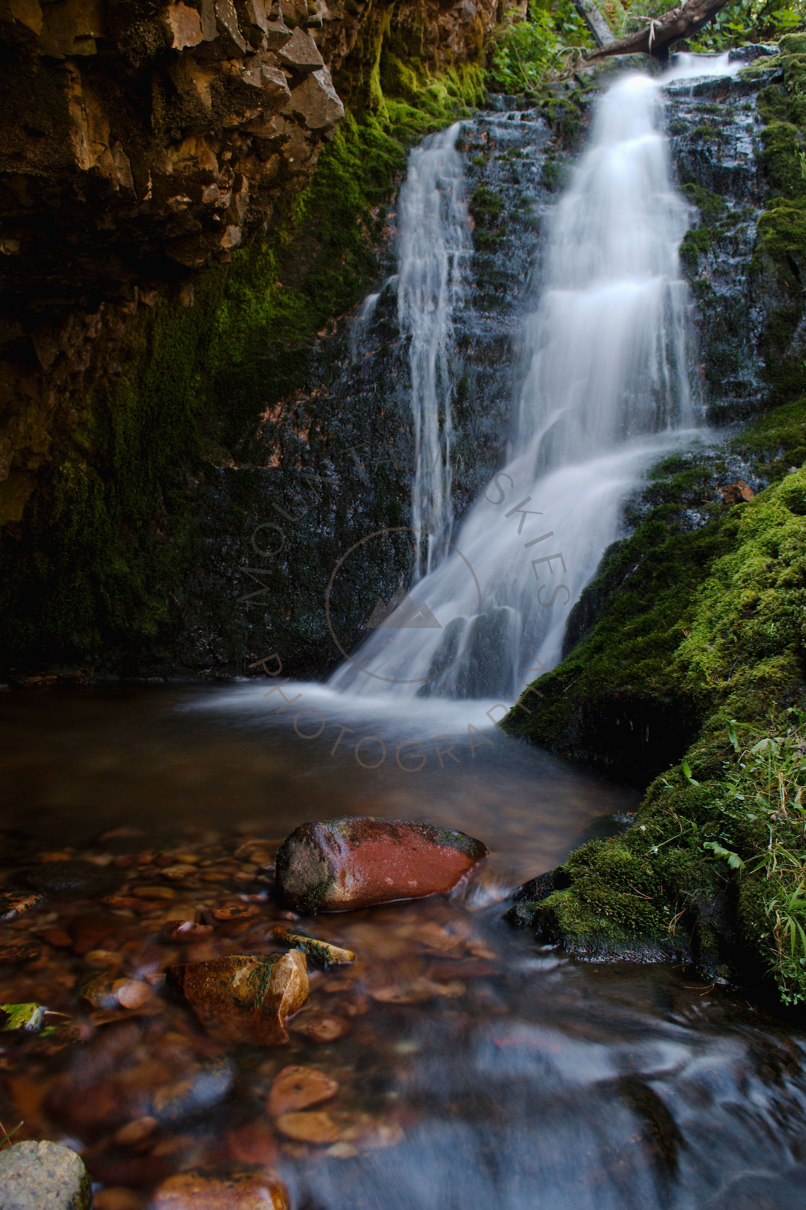 Waterfall flowing over moss-covered rock into a dark pool